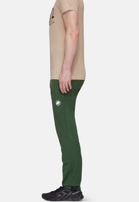 Groene sportieve broek van rekbaar materiaal, met een zijlogo, slim fit en een gladde textuur, gecombineerd met zwarte schoenen.