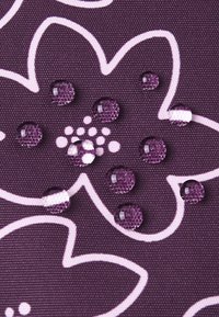 Lilla stof med et blomstermønster i lys pink. Vanddråber er synlige på overfladen, hvilket fremhæver teksturen og det vandafvisende kvaliteter.