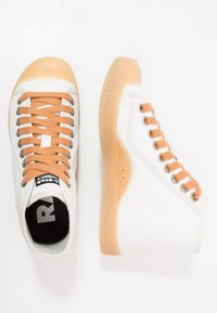 Białe trampki w stylu high-top z beżowymi gumowymi podeszwami i pasującymi beżowymi sznurowadłami, przedstawione z widoków z góry i z boku na białym tle.