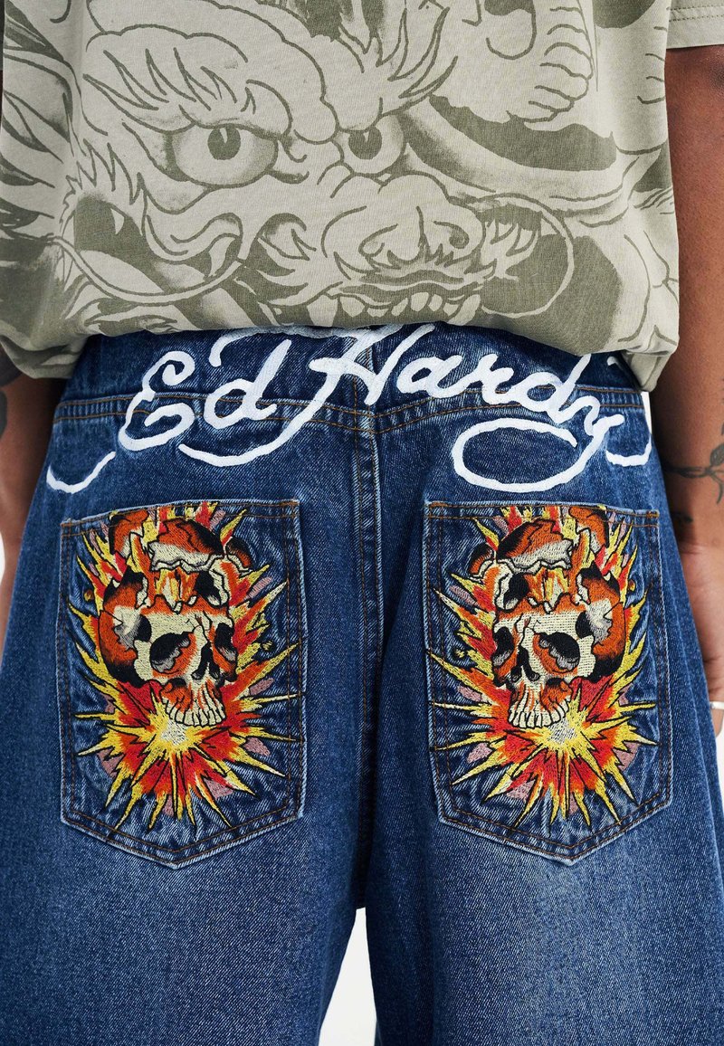 Shorts in denim con ricami di teschi con dettagli di fiamme sulle tasche posteriori. Logo bianco "Ed Hardy" sulla cintura. Colore blu classico.