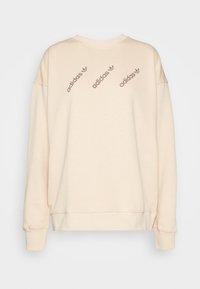 Kremskrāsas džemperis ar garām piedurknēm, apaļu kakla izgriezumu un trim diognālām brūnām Adidas logo uz aizmugures. Mīksta, teksturēta auduma virsma.