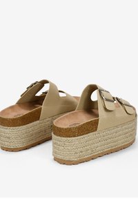 Sandali platform beige con dietro aperto, fasce larghe e fibbie argentate. Suola intermedia intrecciata in corda e plantare in sughero testurizzato. Suola in gomma.