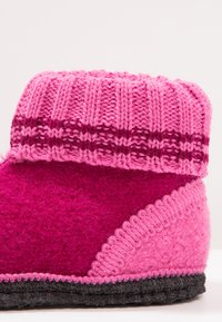 Roze vilten slippers met een gebreide roze en bordeauxrode boord, met een gestructureerde oppervlakte en een contrasterende donkere rubberen zool.