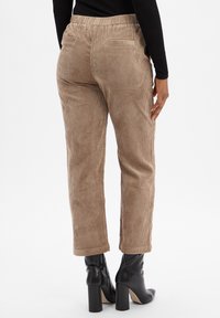 Spodnie z korduroyu w jasnobrązowym kolorze z fakturalnym wzorem pionowych pasków. Posiadają elastyczny pas i dwie tylne kieszenie. Noszone z czarnymi botkami na obcasie.
