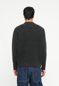 Dark gray ribbed sweater with a round neckline, long sleeves, and a relaxed fit, made from textured knit fabric. Plain back design.