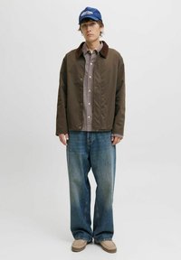 Bruine nylonjack met een corduroy kraag, geruit overhemd, losse blauwe denim jeans en beige moccasinschoenen, aangevuld met een blauwe pet.