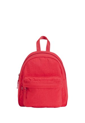 Petit sac à dos rouge avec un compartiment principal zippé, une poche avant zippée et une anse de transport supérieure sur fond blanc.