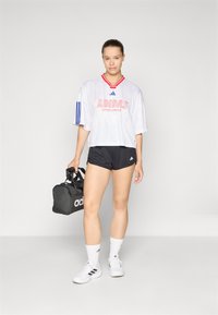 Witte T-shirt met korte mouwen van Adidas met rode accenten, zwarte shorts, zwarte sporttas en witte sneakers, die een sportieve, functionele uitstraling tonen.
