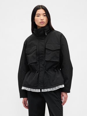 Sort jakke med høj krave, der har to forlommer, en snøre i taljen og en blondekant forneden. Struktureret stof.