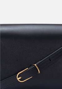 Gros plan d'un sac en cuir noir avec une bandoulière ornée d'une petite boucle en or et d'une boucle.