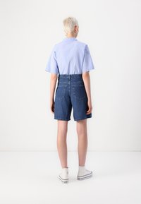 Modra prugasta srajca s kratkimi rokavi, v kombinaciji z visokim pasom denim kratkimi hlačami. Bele superge dopolnjujejo sproščen look.