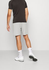 Svart kortärmad träningsskjorta med strukturerade axlar, matchad med ljusgrå shorts. Modellen bär vita sneakers och strumpor.