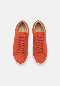 Red suede sneakers with a round toe, six eyelets, tonal laces, and white rubber soles. The interior is beige with minimal branding.