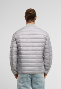 Lysegrå dunjakke med horisontalt quiltet design, ribbet krave og elastiske manchetter, parret med lyse denim jeans.