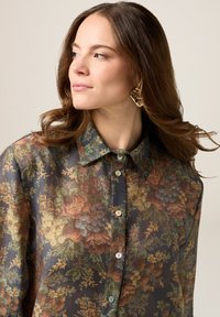 Koszula w kwiatowy wzór z ciemnego materiału z wielokolorowymi kwiatami. Oferuje kołnierzyk i zapięcie na guziki z jasnymi guzikami.