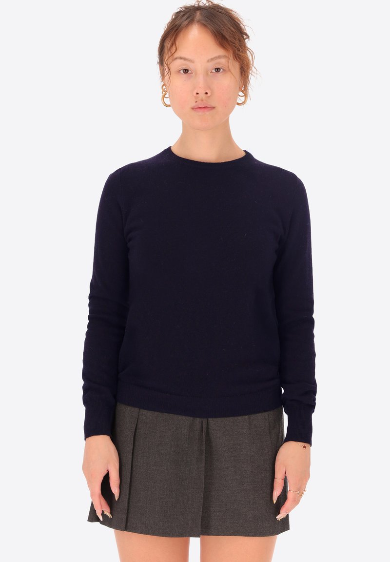 Maglione blu navy realizzato in un morbido tessuto testurizzato con scollo rotondo e orlo a coste, abbinato a una gonna grigia plissettata.