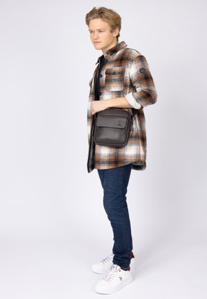 Camicia a quadri marrone e bianca, jeans blu scuro e sneakers bianche. Borsa a tracolla in pelle marrone scuro con patta e zip.