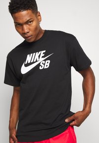 Black Nike SB t-shirt made of cotton, featuring a white logo in a bold font across the chest, short sleeves, and a round neckline.