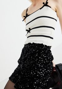 Vit ribbad linne med svarta horisontella ränder, prydd med små rosetter, tillsammans med en svart paljettminikjol.