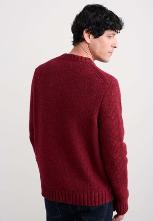 Suéter de punto rojo con un acabado texturizado, cuello y dobladillo acanalados, que presenta un corte clásico y ligeros destellos de color en toda su superficie.