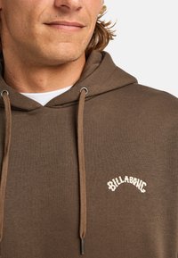 Brauner Baumwoll-Hoodie mit einem gestickten weißen Logo, ausgestattet mit einer Kapuze mit Kordelzug und einer glatten Textur.