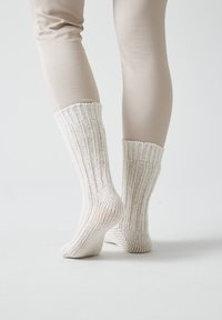 Calcetines blancos de punto con un patrón acanalado, que presentan un diseño texturizado. Se elevan por encima del tobillo, sujetos de forma segura en la parte superior.