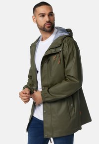 Jachetă waterproof verde cu glugă gri, având manșete elastice, închidere cu fermoar și capse, și buzunare frontale cu accente de cusătură contrastante.