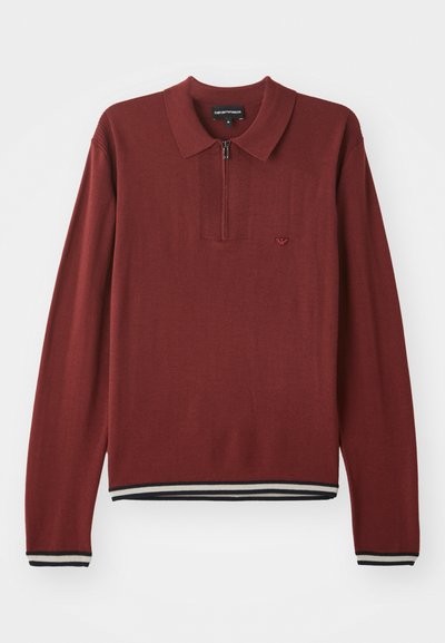 Tricou polo lung cu mânecă lungă, de culoare cărămizie, cu guler cu fermoar, având tiv și manșete ribbed cu dungi bleumarin și alb, realizat dintr-un material moale.