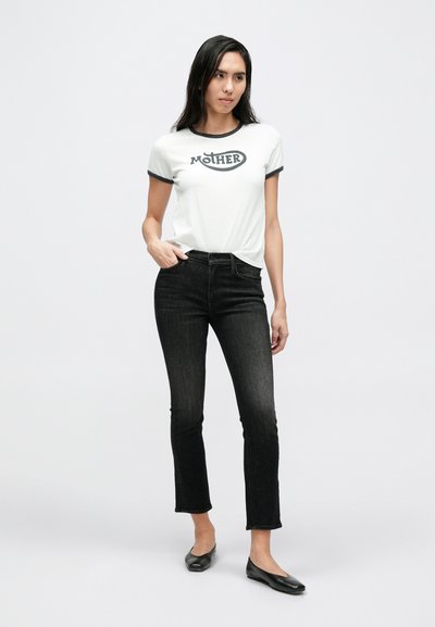 Fehér rövid ujjú póló fekete szegélyű gallérral és "MOTHER" felirattal, fekete magasderekú farmernadrággal és fekete balerinacipővel párosítva.