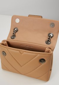 Sac à main en cuir beige avec un motif en chevrons matelassé, quincaillerie en ton argenté, fermeture à pression et un intérieur spacieux, affichant une étiquette de la marque à l'intérieur.