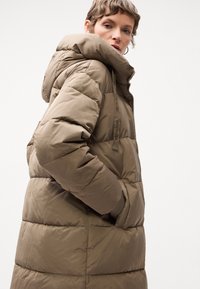 Padded winter coat in olive green, featuring a high collar, hood, side pockets, and ribbed cuffs. Smooth, glossy texture with quilted details.