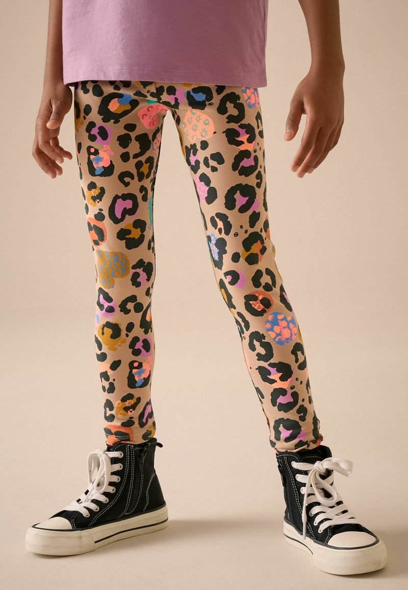Bambino che indossa leggings colorati con stampa leopardata, sneakers alte nere con lacci bianchi e una maglietta viola visibile in vita.
