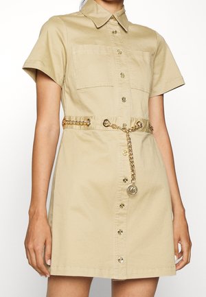Beige kortærmet kjole med knapper, to brystlommer og et guld kædebælte med en rund MK logo vedhæng.