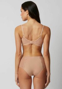 Reggiseno beige con schiena in pizzo e spalline regolabili, coppe lisce, e culotte a vita alta abbinate con dettagli in pizzo sui lati.