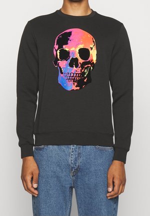 Czarna koszula z długim rękawem z dużą, kolorową grafiką czaszki na piersi, noszona z niebieskimi jeansami.