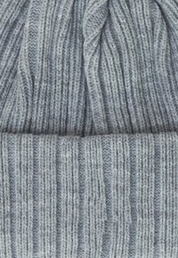 Berretto grigio lavorato a maglia con una texture a coste, caratterizzato da linee verticali e una parte superiore arrotondata. Realizzato in morbido filato spesso per garantire calore.