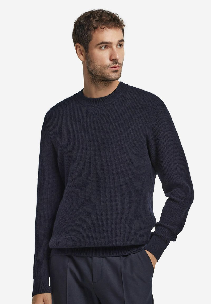 Marinblå stickad tröja med en texturerad ribbad design, rund halsringning och långa ärmar. Har en avslappnad passform vid fållen och ärmsluten.