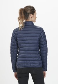 Marinblå pufferjacka med en lätt, vadderad design, hög krage och elastisk nederkant. Har en slät, glänsande yta och långa ärmar.