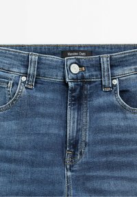 Mörkblå denimjeans med en slät yta, silverknappstängning och gula sömmar. Tagg synlig med "Massimo Dutti"-märke.