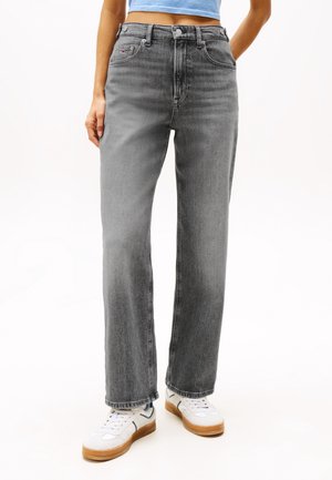 Person wearing faded gray straight-leg jeans, white sneakers with gum soles, and a cropped light blue top, standing against a white background.