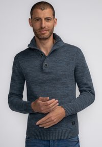 Suéter de punto azul oscuro con un cuello alto, dos botones grandes y puños y dobladillo acanalados. La textura es ligeramente moteada.