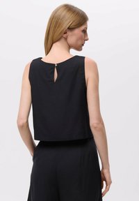 Zwarte mouwloze top met een ronde halslijn, cropped design en een kleine sleutelgatopening aan de achterkant, inclusief een knoopsluiting.