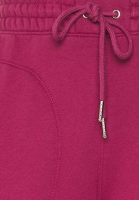 Fuchsia joggingbroek heeft een tailleband met trekkoord en zilveren accenten, een zachte textuur en een zijzak met een subtiele afgeronde naad.