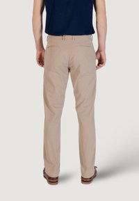 Pantaloni beige dritti con una consistenza liscia, dotati di due tasche posteriori. Indossati con una camicia blu scuro e scarpe marroni.