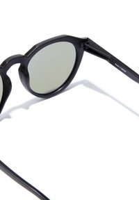 Crne okrugle sunčane naočale s mat završnom obradom, sivim lećama i blago debelim geometrijskim okvirom. Nastavak ima ugraviranu oznaku "Made in Spain".