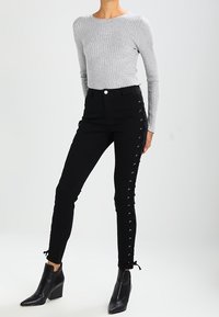 Svarta skinny jeans med snörningsdetaljer på sidan, kombinerat med en ljusgrå ribbad långärmad topp och svarta klackanvända stövletter.