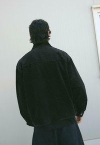 Jachet�ă din catifea neagră cu o croială lejeră, având guler și manșete cu nasturi, material texturat și detalii de cusătură întărită.