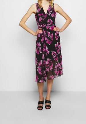 Ärmelloses schwarzes Midikleid mit pinkem und violettem Blumenmuster, V-Ausschnitt, Wickelstil, getragen mit schwarzen Sandaletten mit Absatz.