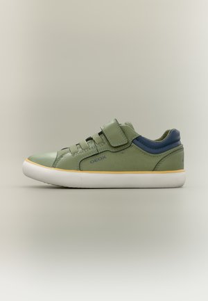 Nízký zelený teniska s námořnicky modrou patou, žlutým lemováním, bílou podrážkou, suchým zipem a tkaničkami, boční pohled na neutrálním pozadí.