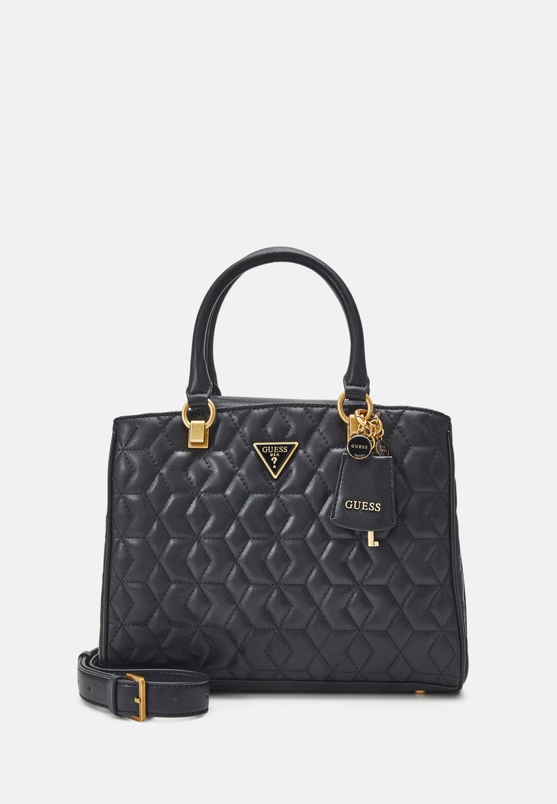 Sac à main matelassé noir Guess avec deux poignées, ferrures dorées, breloques logo et une bandoulière amovible sur fond uni.